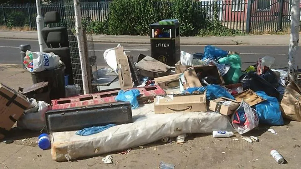A skip overflowing with furniture and rubbish, with more waste and black bin bags dumped on the pavement beside it