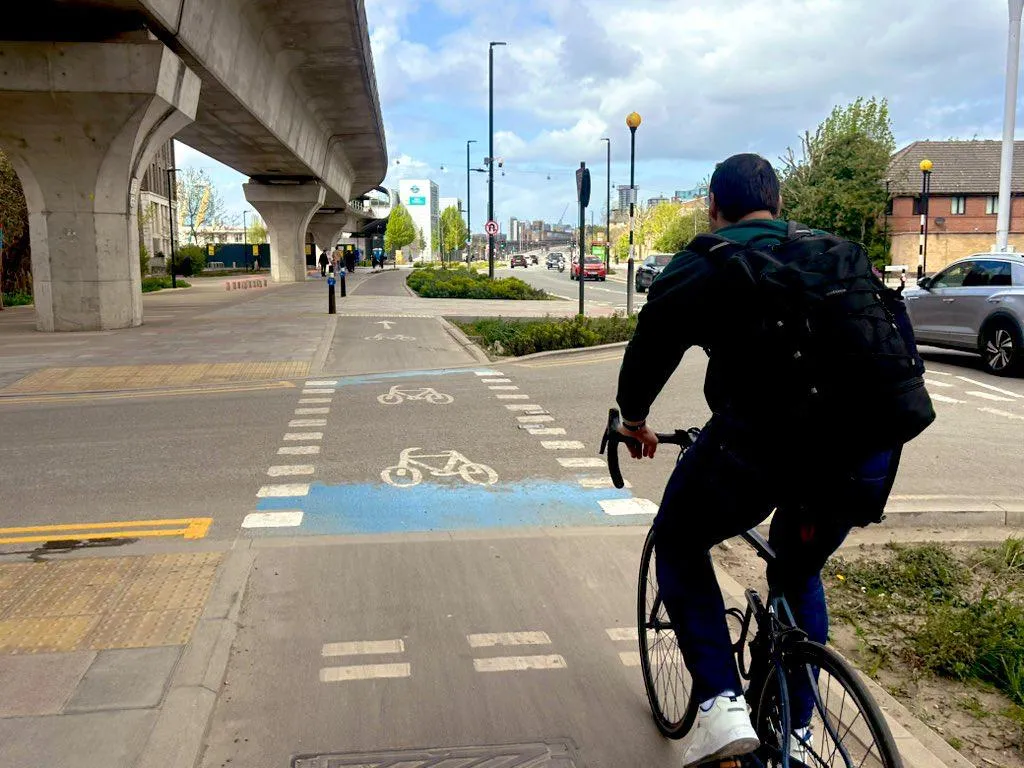 John Morris cycling along a segregated cycle lane on the Royal Docks Corridor, with the DLR viaduct overhead